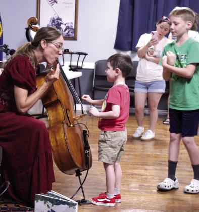Zane Dowell, 4, of McLoud, plucks the strings on Erin Yeaman's cello and gets a reaction during the 'Tunes and Tales with Erin Yeaman' McLoud Public Library program, held on June 18 at the Ray Large American Legion Post 244. Yeaman also played her cello along to three children's books and read 'The Three Little Pigs,' as volunteers made sound effects. In addition to being a composer and voice actor, Yeaman provides music for Scholastic audio books.