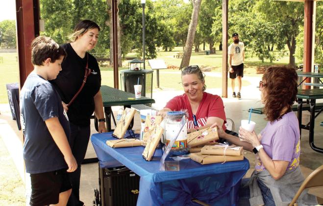Luke Webb, 10, of Tecumseh, makes his selection in the Tecumseh Public Library "Blind Date with a Book" fundraiser, with the help of mom, Becky Webb, Jennifer LaGrange, and library associate Cyndi Seeley during the "Rolling Thunder Book Bus" program, held at Slick Humphrey Park on June 18. The library has children's books covered with paper which only state their genre, available for a donation of $5. The book bus was also at the park with free books for those in kindergarten through fifth grade.