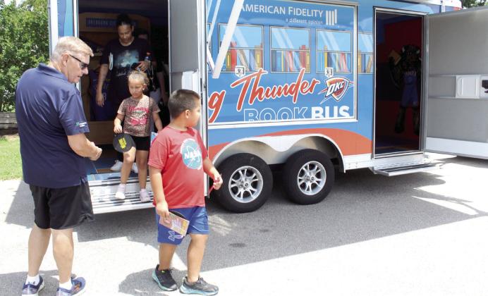 Gavin Klippenstine, 8, and Genesis Robbins, 5, emerge from the Rolling Thunder Book Bus with free books, as John Stewart hands out bookmarks.