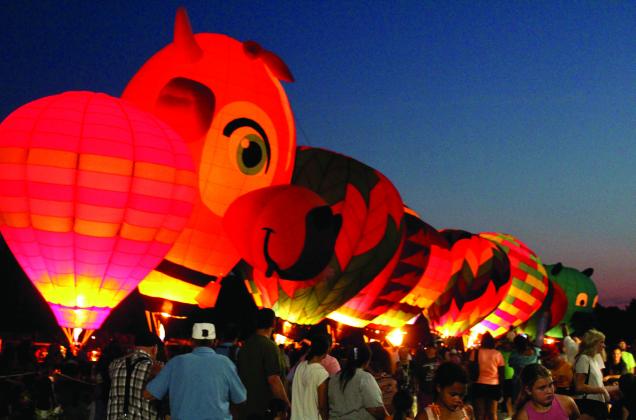 A line of hot air balloons light up on Aug. 9, 2025 - including "Milky Way," which is shaped like a cow, and a new llama-shaped balloon - during the FireLake Fireflight Balloon Festival at the CPN Festival Grounds. File photo