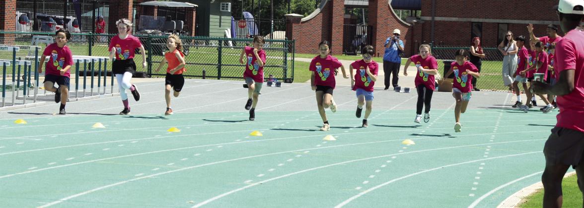Students in first through sixth grade race during the Health Week Track Clinic, as former track star Charles Clark, far right, watches, at Oklahoma Baptist University on May 28. There were 48 students who participated in two sessions, said Macy Muirhead with Pottawatomie Go (POGO). Photos by Natasha Dunagan, Countywide &amp; Sun