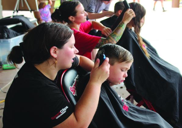 Sport Clips hair stylist Nicole Lawless talks with Keanu Christensen, 4, of Shawnee, before shaving his sideburns during the Second Annual Hug-a-thon, held at Woodland Veterans Park in Shawnee on Aug. 2. Also giving free haircuts were stylists Brittany Burden and Libertee Desordi. Natasha Dunagan, Countywide &amp; Sun