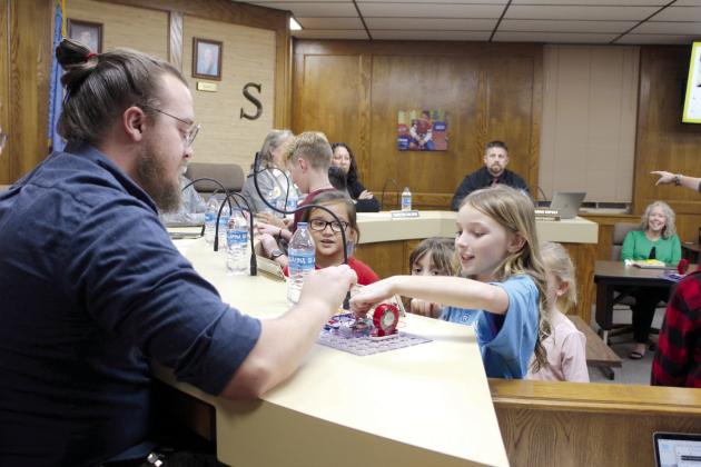 Third-grader Whitlea Espolt and other Will Rogers Elementary students show a circuit board they made to Shawnee Board of Education member Turner Bass during the Dec. 4 meeting. Several students in the gifted and talented after-school program demonstrated their projects.