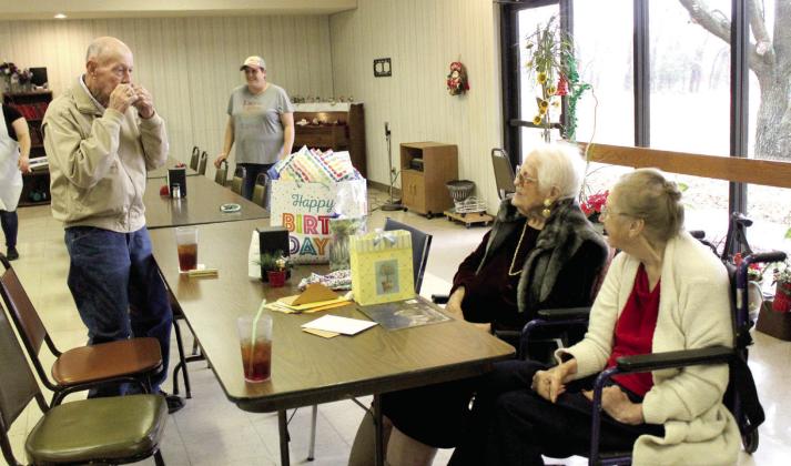 Ed Medcalf, age 93, plays a harmonica his grandmother gave him at age 6, and sings “Have I Told You Lately That I Love You,” to his friend Clemmie Lucas during her early 100th birthday party on Dec. 15. Lucas will turn 100 on Christmas Day, and Project H.E.A.R.T, in conjunction with the Tecumseh Senior Center, hosted her birthday party. Also shown, far right, is Lucas’s friend, Charlotte Harrison. Countywide &amp; Sun/Natasha Dunagan