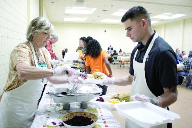 Melissa Hewett, who is Randy Gilbert's cousin from Arkansas, adds cranberry sauce to dinners held by volunteer Mason Blumenthal at the 19th Annual Tecumseh Family Thanksgiving Dinner, held at Tecumseh City Hall Auditorium on Nov. 28. Blumenthal is also in the Army and volunteered for the first time at the event with his father, John, and grandmother, Louise. Countywide &amp; Sun/Natasha Dunagan