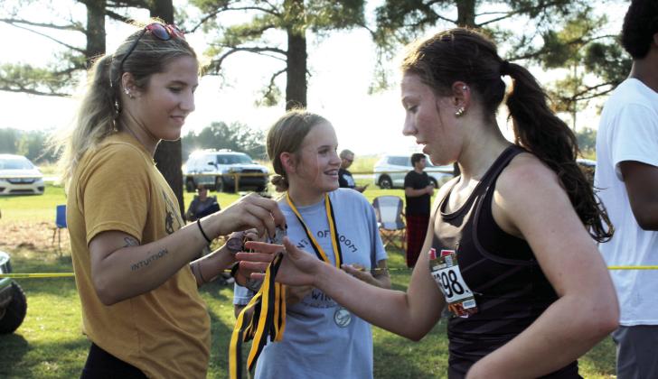 North Rock Creek freshman Evy Simpson receives her medal from Tecumseh Junior High Cross Country Coach Elizabeth Robinson during the 2025 Savage Cross Country Invitational on Sept. 23. Robinson placed 16th out of 49 high school girls. See full caption below.