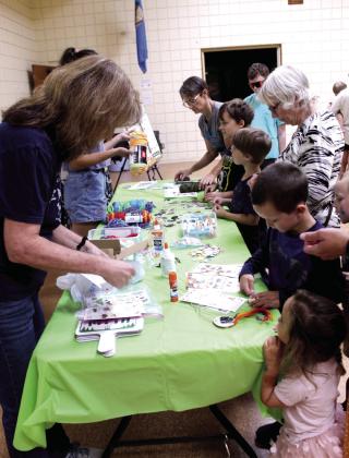 Children and adults create animal-themed necklaces with the help of Wild Care Oklahoma representatives Kristy Wicker and Iris Hoyer during the "Misunderstood, Not Mean: Skunks, Coyotes &amp; Other Wild Neighbors" Tecumseh Public Library program on July 22.