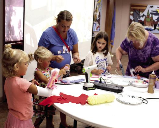 Maci Geissler, 5, of Shawnee, far left, tries out her rainbow unicorn sock puppet, as her sister, Mary Geissler, 4, and mother, Lana Geissler, continue working, during the "Creativity Unleashed: Crafternoon for Kids" program on July 22. Also shown are Vayda Bullen, 7, of Shawnee, and her grandmother Tiia Bullen.