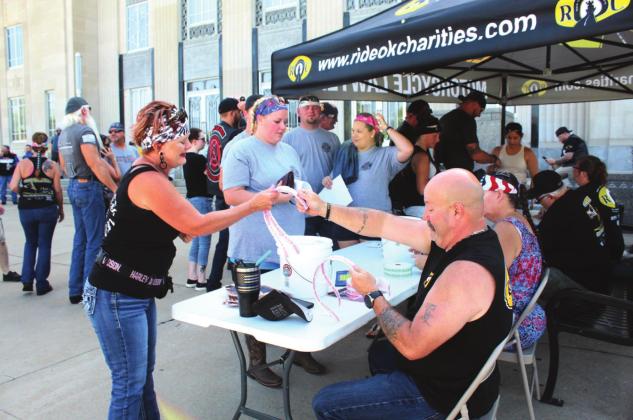 Grady County Deputy Mark Asche, with Ride Oklahoma Charities, hands a strip of tickets to Starla Ellison, of Choctaw, after she registered for the Justin Terney Memorial Poker Run on July 23. About 78 motorcyclists and three vehicle drivers participated in the event. Countywide &amp; Sun/Natasha Dunagan