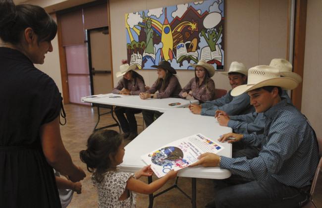 Tatum Roberts hands Marie Blankemeyer, 4, of Shawnee, a poster after he and five other IFYR contestants/youth directors signed it. Also shown, from left, are Ryla Bryant, Sadie Noles, Jasey Graves, A.W. Southern and Kruz Cartwright (hidden).