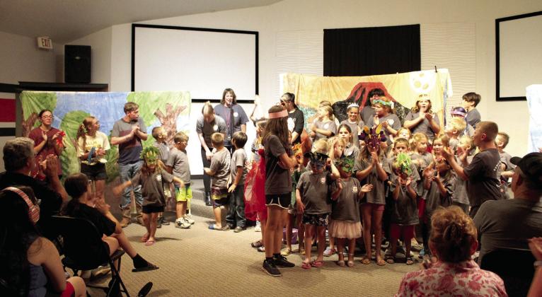 As Macomb Summer School Director Shannon Browning speaks, 58 students applaud their director and theatre teacher Kendra Johnson following their play, "Attack of the Evil Bugs," presented at the Student Center on July 13. The play was written by the students, who also designed and painted backdrops on plastic tablecloths and made fliers. Johnson said the pre-K through fifth-grade students spent the last seven weeks working on the play, and she tried to make the experience fun so they wouldn't lose interest.