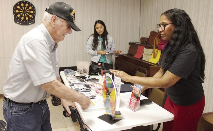 Raymond Atkinson spins a wheel to win a prize at the Absentee Shawnee Housing Authority booth. Assisting Atkinson is Breeahnna McCarver, and Tara Wallace is also shown.