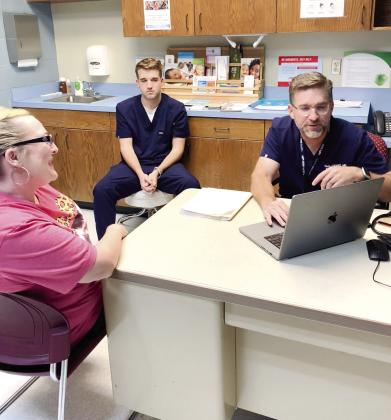 Dr. Scott Stewart talks with Kelly Long, a patient at the Pottawatomie County Volunteer Health Clinic, as his son and medical scribe Parker Stewart looks on, May 11. Stewart also volunteers at the clinic with his other son, Reid, not shown, who screens patients and helps in the pharmacy. Photo provided by Sharon Gerards.