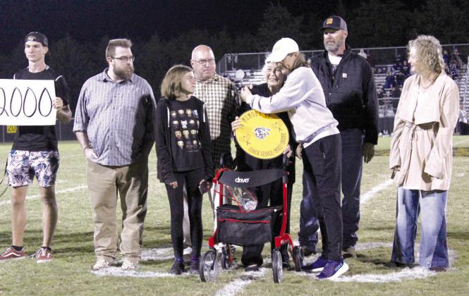 Judy Snider, the wife of late Tecumseh Tennis Coach George “Mike” Snider, gets a hug from current Tennis Coach Jennifer McKnight, as Snider’s sons Greg and Blake and other family members look on. Coach Snider was memorialized with a sign that will hang on the tennis court fence during the Oct. 12 home football game.
