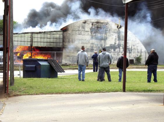 While firefighters work to put out the fire from the south side, others including Fire Chief Rhett Banks, second from left, watch over a fire at the Jordan Contractors, LLC mechanic shop in downtown Tecumseh on May 6. Several explosions were heard during the fire. Cheyanna Dietz, Countywide &amp; Sun Intern