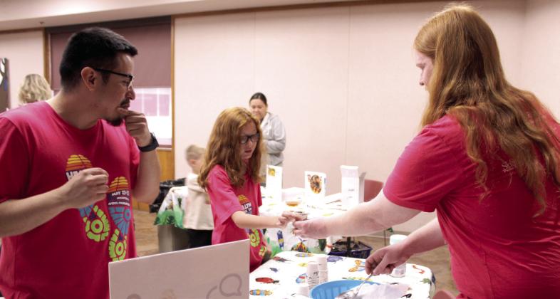 Shawnee Children's Librarian Logan Moore, far right, hands a sample of fried mealworms to Killian Keathley, 12, of Shawnee, as fellow librarian Jairo Montelongo looks on, during Bugfest at Shawnee Public Library on May 30.
