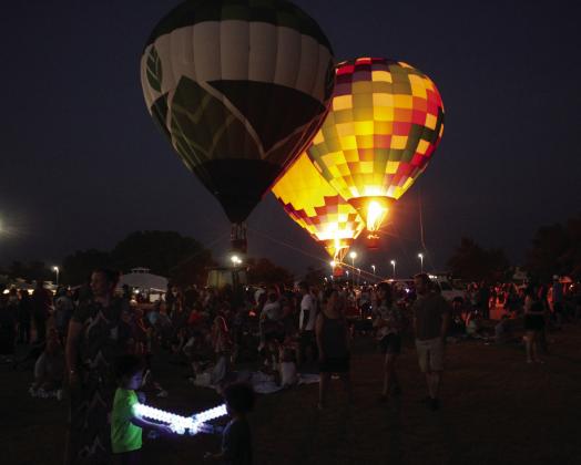 Two hot-air balloons light their fires, as two children play with light-up toys, during the balloon glow on Friday night, Aug. 7, during the FireLake Fireflight Balloon Festival.