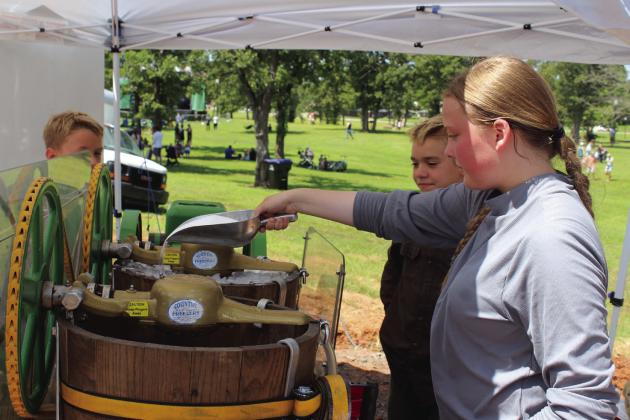 Makayla Combs of Ohio adds rock salt to the ice in an ice-cream maker which is run by a 1939 John Deere hit-and-miss engine at Poppin' Johnny's Ice Cream during the McLoud Blackberry Festival on June 21. The machine is owned by Jonathan Hilbun of McLoud and can produce five gallons of ice cream per barrel. Also shown watching are brothers Benjamin and Stephen Tiller of Mustang. There were 80 vendors at the festival this year, plus those with the carnival company, said Melanie Krause with the McLoud Chamber.