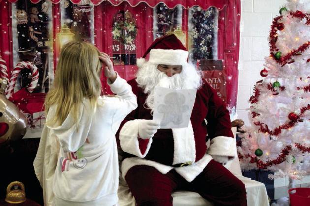 Santa looks at a coloring page completed by Lilly Hampton, 8, of Shawnee, during the Second Annual Breakfast with Santa, held at Shawnee Middle School on Nov. 30. The event was a fund-raiser for the Shawnee Wrestling Program and also included breakfast served by the wrestlers, reindeer ring toss, backgrounds for selfies and coloring stations. Countywide &amp; Sun/Natasha Dunagan