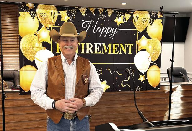 Mike Booth poses in front of his retirement banner during the party held in his honor Dec. 30, 2024. Booth served as Sheriff for 16 years. Countywide &amp;amp; Sun/Suzie Campbell