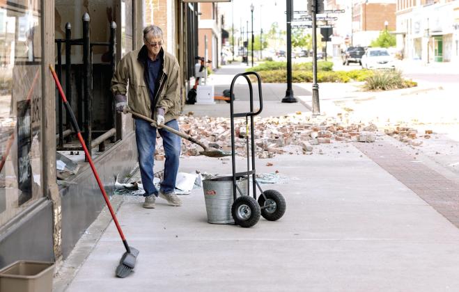 A Shawnee citizen sweeps and clears debris from in front of the Pott County Book Store in downtown Shawnee following the tornado Wednesday night. The front glass of the store as well as the west wall on the second floor was busted out or ripped from the building. Photo provided