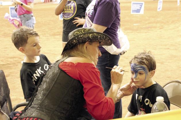 'Annie Heart' (Valarie Hames), with Creative Magic Productions in Bethel, paints the face of Jameson Sedlock, 4, as his brother, Roman Sedlock, 6, both of McLoud, watches during Relay for Life of Pottawatomie County, held at the Heart of Oklahoma Expo Center Fred Humphries Arena on May 29. In addition to face painting, 'Jack Spade' (Jeff Hames) juggled and twisted balloon animals that evening.