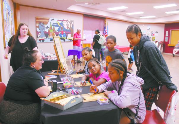 The Banks family of Shawnee take turns writing their names in hieroglyphics on papyrus bookmarks, as Mabee- Gerrer Museum of Art Director of Development Sylwia Partyka looks on. Shown, seated from left, are Andrinee, 11, Micelea, 9, and Andrea, 13, standing, Ronald, Jr. and Ronjnae, 14, Banks. Natasha Dunagan, Countywide &amp;amp; Sun