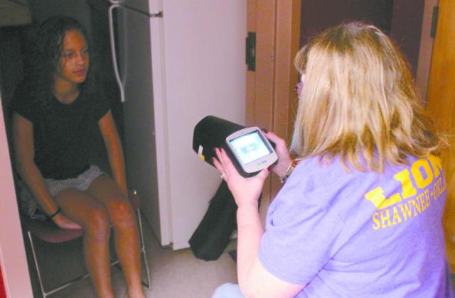 Shawnee Lions Club Vice President Debbie Coym uses an instrument to detect eye problems with Kaylin Burdine, 10, of Shawnee, during the 'Making a Difference: School Prep for Success' event at the Shawnee Public Library on Aug. 9. The Lions Club takes donations of old glasses and now hearing aids, said Lions Club Secretary Butch Lutonski. Natasha Dunagan, Countywide &amp;amp; Sun