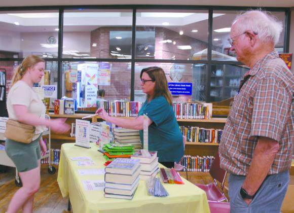Carmen Wolf of the Friends of the Shawnee Library hands information about their October book sale to Grace Randolph, as fellow FOSL member Bill Hagen looks on. Natasha Dunagan, Countywide &amp;amp; Sun