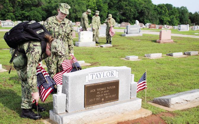 Lead Cadet Petty Officer Second Class Diana Murray uses a screwdriver to prepare the ground for a flag to be placed at the grave of a veteran on May 20 at the Tecumseh Cemetery. Seaman Recruit Tiffany Porter looks on.