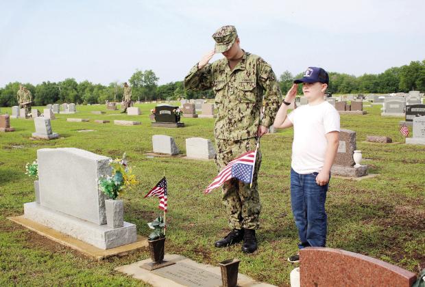 Petty Officer Third Class Callan Weathington and Recruit LC1 Gabriel Synakowsky, 10, salute a flag placed on the grave of a veteran.