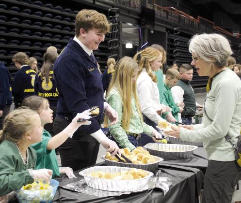 Tecumseh 4-H members Jessi Peacock and Adalyn Seaton and North Rock Creek FFA member Gus Goodson serve Delinda Curtis rolls and butter during the 34th Annual Pottawatomie County Junior Livestock Show Pig Roast and Trophy Auction in 2023. File photo