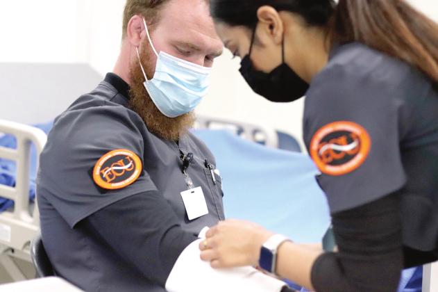 ECU Nursing student Gabriel Rebischke sits patiently while fellow student Suja Shresta practices applying bandages to his arm.