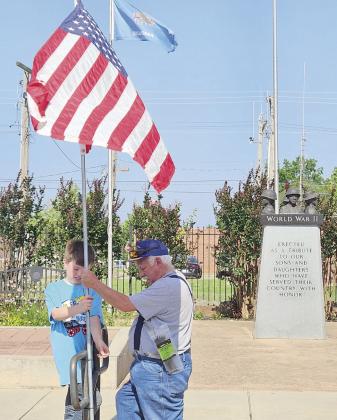 Daryl Murray, 9, zip ties a flag to a hand rail in front of the veterans memorial beside Tecumseh City Hall on Flag Day, June 14, as his grandfather Tom Snodgrass helps to hold it in place. Snodgrass is the Commander of American Legion Post #260 in Tecumseh, and they displayed 30 flags around Tecumseh for the holiday. Photo provided.