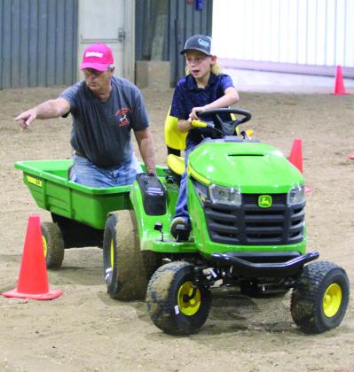 Dace Dockrey, age 9, drives a garden tractor through the obstacle course of the Peewee and Midget Tractor Operator Contest, as Fair Board Member Lynn Marlow, points to where he needs to go, on Sept. 6 at the Pottawatomie County Free Fair. File photo