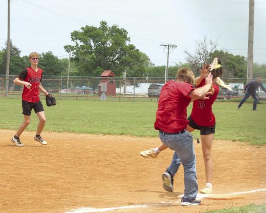 Fifth-grade teacher Sam Adams runs to first base, as slow pitch player RyLee Hancock makes the catch, and Macomb baseball player Connor Hutchins watches the action.