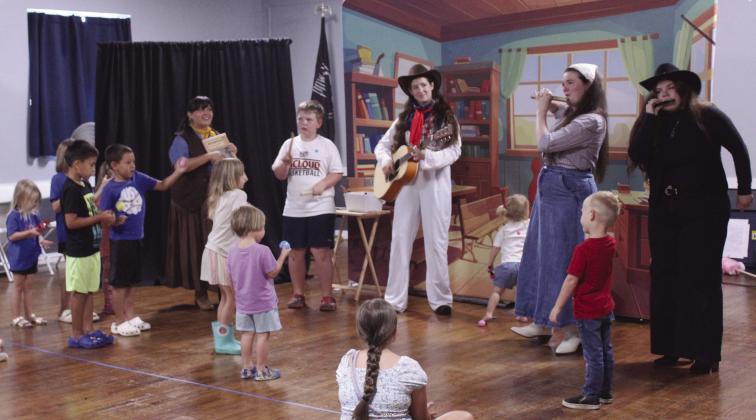 "Tam," played by Olivia Flores, works the washboard; "Pop Magano," played by Savannah Gordon, strums guitar; "Pam," played by Sarah Spurlin, performs on the magic flute; and the "Queen of Knocked Sara Stro," played by Cheyenne Holland, makes music on the harmonica, as children in the audience harmonize on percussion instruments.