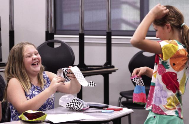 Pottawatomie County 4-H Club member Nova Harrison, left, has a laugh with a friend while making a duct tape pencil pouch during the "Fair Project Day" meeting, held at North Rock Creek High School on Aug. 4.