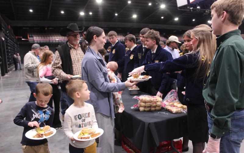 Tecumseh FFA members serve a family, as Asher 4-H member Jack Jett, far right, waits to help carry plates, during the 37th Annual Pottawatomie County Junior Livestock Show (PCJLS) Pig Roast and Trophy Auction, held at FireLake Arena on Feb. 2. Shown serving, from left, are Harrison Kinsey, Sawyer Spears, Landyn Seaton, Porter Neil, Abbi Jordan and Rylee Chaffin. Natasha Dunagan, Countywide &amp; Sun