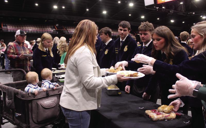 Tecumseh FFA Members Abbi Jordan and Rylee Chaffin add rolls to the plates of Chelsi Peacock, of Tecumseh, as her nine-month-old twins, Gavin and Greyson Pell, sons of Tecumseh FFA Advisor Corey Pell, wait in their cart during the 37th Annual Pottawatomie County Junior Livestock Show (PCJLS) Pig Roast and Trophy Auction, held at FireLake Arena on Feb. 2. Also serving, from left, were Sawyer Spears, Landyn Seaton and Porter Neil. Natasha Dunagan, Countywide &amp; Sun