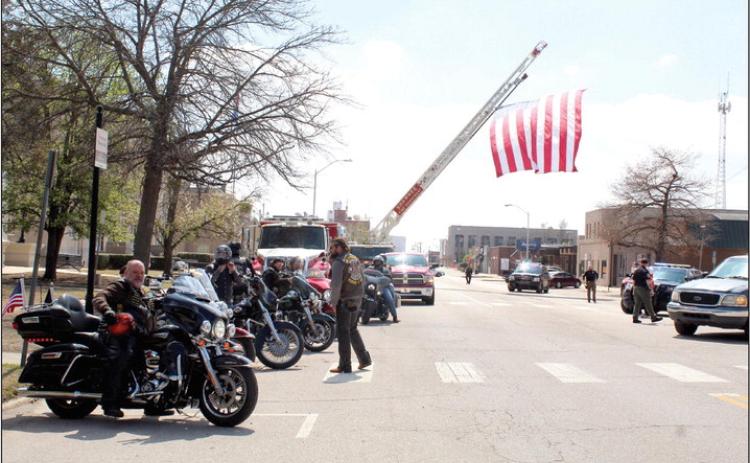 Bikers in the Seventh Annual Ruben Rivers Medal of Honor Ride park in front of the Woodland Veterans Park, March 25, as a 20'x30' U.S. flag hung from a Shawnee Fire Department ladder flies over Broadway Ave. Roll to Wreaths Riders 4 Vets President and Founder Rowdy Butler is shown far left. Countywide & Sun/Natasha Dunagan