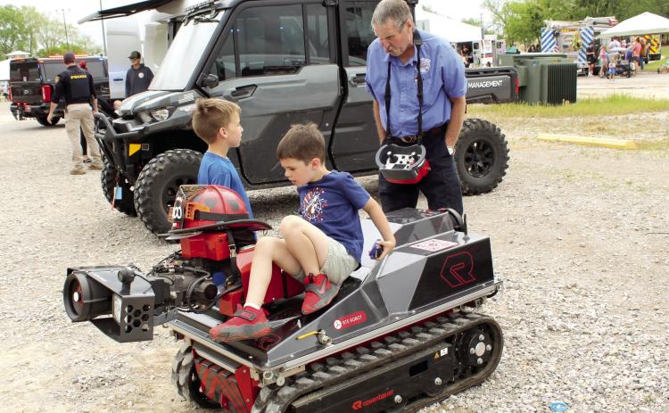 Hunter Elmore, 8, standing, talks with Rosenbauer dealer Mark Hardy about the remote control robot firefighter, as Troy Palmer, 5, sits on it, during Touch-A-Truck and Beyond, held at the CPN Festival Grounds on April 11 and organized by Pottawatomie County Emergency Management. Both boys are from Shawnee. Photos by Natasha Dunagan, Countywide & Sun