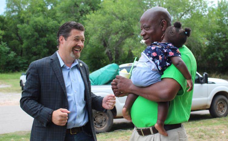 Epic Sno Cones owner David Henry, right, holds his sleeping granddaughter, Safiya Henry, 9 months, and eats a Mississippi Squirrel snow cone, as he talks with Oklahoma Senator Shane Jett on July 3. Shawnee’s oldest snow cone stand, at 722 S. Beard, was set to have their grand re-opening that day, but the electricity went off. They will announce when the event will be rescheduled.