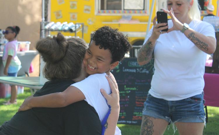 Exzavier Beal, 7, of Shawnee, hugs his mom, Kayla Beal, to make a "Forever Hug" with his arms painted white and hers blue during the First Annual Hug-A-Thon held at Woodland Veterans Park on Aug. 3. Also shown, recording the moment, is Exzavier's aunt, Rita Beal. Countywide & Sun/Natasha Dunagan