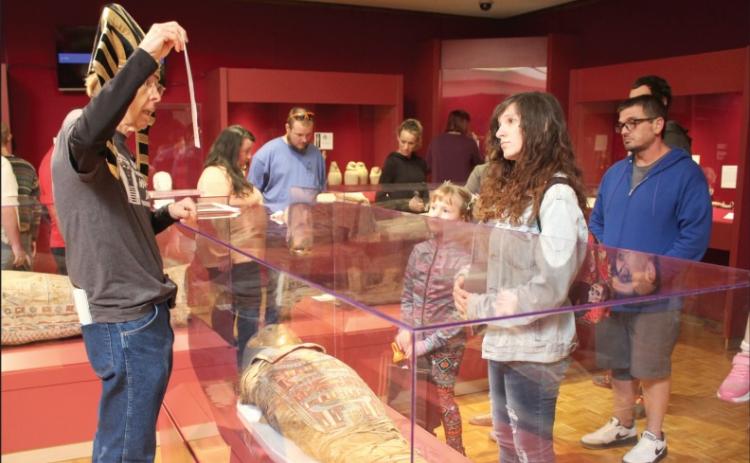 Dressed in a pharoah hat, Mabee-Gerrer Museum of Art Docent Dick Trim speaks about the mummification process, as Princess Tutu lays in front of him, during Mummy Day at the museum on Oct. 26. Tutu was mummified in 332 B.C. in the Faiyum district of Egypt, and was gifted to the Glen Island Museum in 1898, according to https://www.mgmoa-gallery.com/tutu-mummy-cnxk. When that museum went bankrupt, Father Gregory Gerrer purchased Tutu at auction. The MGMOA also has an unidentified mummy from the Roman era.