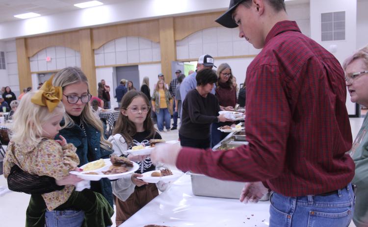 Tecumseh FFA student Lyric Morrison, far right, adds brownies to the plates of Huxlee Newell, 2, of Yukon; THS 2016 grad Hunter Newell; and Presleigh Scott, 10, during the annual Tecumseh FFA Pig Roast, held at the THS Alumni Center on Nov. 21. FFA Advisor Mara Carmen said they sold 225 tickets for the fundraiser. Photos by Natasha Dunagan, Countywide & Sun