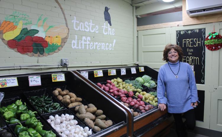 Crows Farm Markets Co-Owner Claudia Crow poses next to the vegetables grown on their farm by her husband, Ricky Crow. C. Crow said a woman who worked at the market painted the mural, and they stand by the statement that home-grown vegetables have more flavor than those from big-box grocery stores. Crows Farm Market in Shawnee will close at the end of this month after 25 years under the Crows' ownership. Natasha Dunagan, Countywide & Sun