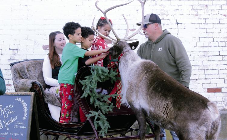 Titus Hancock, 6; Malachi Hancock, 5; and Emersyn Hancock, 7, all of Meeker, pet Rose the Reindeer, as Jamie Hancock and reindeer wrangler, Nick Ledbetter, watch and supervise at The McLoud Mercantile on Dec. 20. Rose comes from the Reindeer Club in Bristow, and Mercantile co-owner Samantha Sessums said in a video on their Facebook page that she has been trying for three years to get the live reindeer there. This year, there was a cancellation and a last-minute opportunity.  See full cutline below.