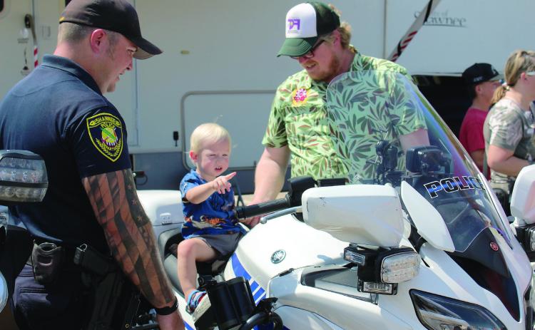 Finley Fry, 17 months, of Shawnee, sits on a Shawnee Police Department motorcycle and points at something, as Corporal Josh Soward, far left, and Fry's father, Matt Fry, keep watch at Cops n' Kids, held on Aug. 24, 2024, at the Heart of Oklahoma Expo Center. File photo