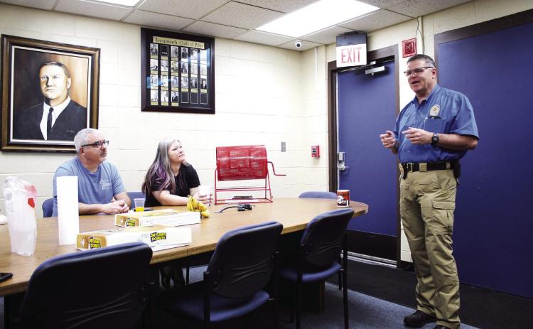 Tecumseh Police Chief J.R. Kidney speaks during the Tecumseh Chamber of Commerce monthly TAG meeting, May 11, as Anthony LaGrange and Kimberly Elliott listen. Behind them is a painting of fallen Police Chief Grover Butler, painted by retired detective Charles Spillers. Countywide & Sun/Natasha Dunagan